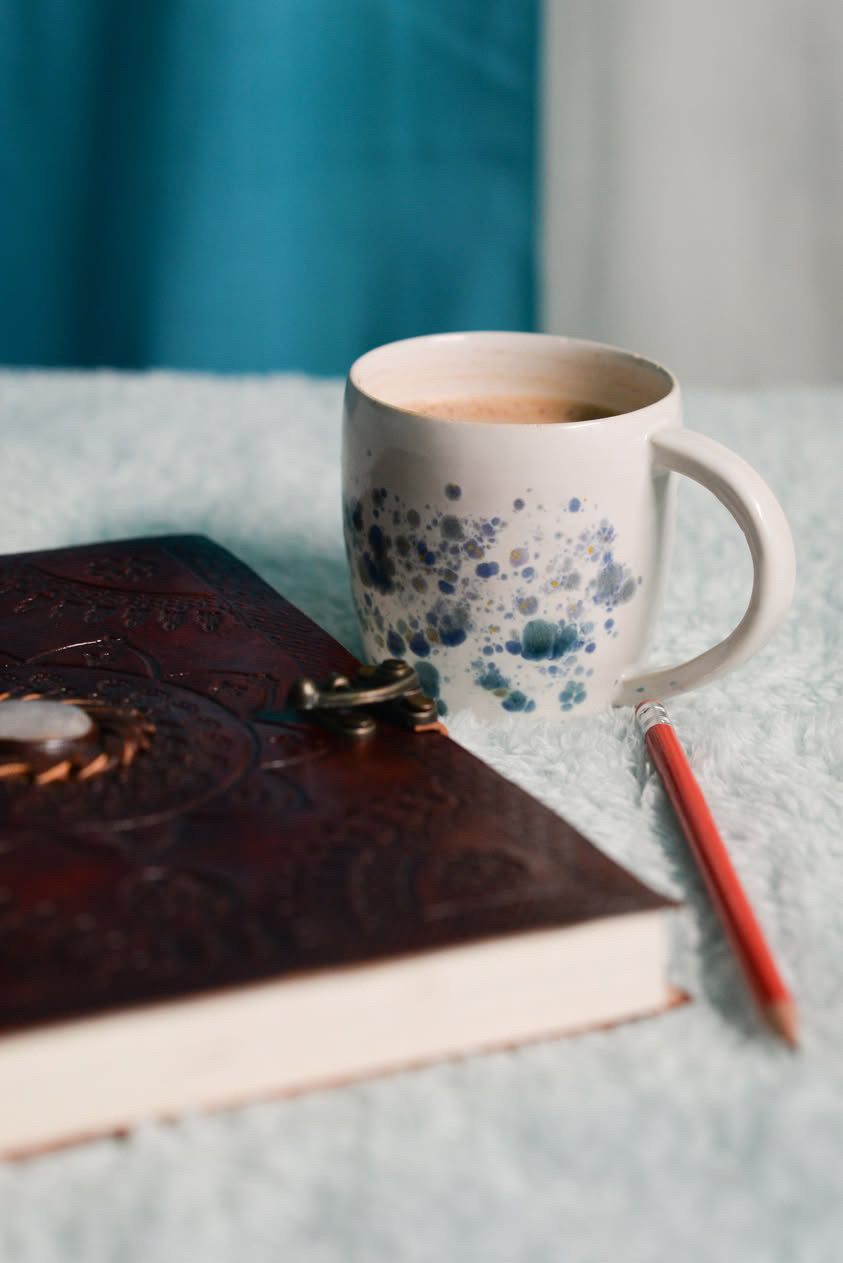 A leather journal beside a cup of coffee and a red pencil