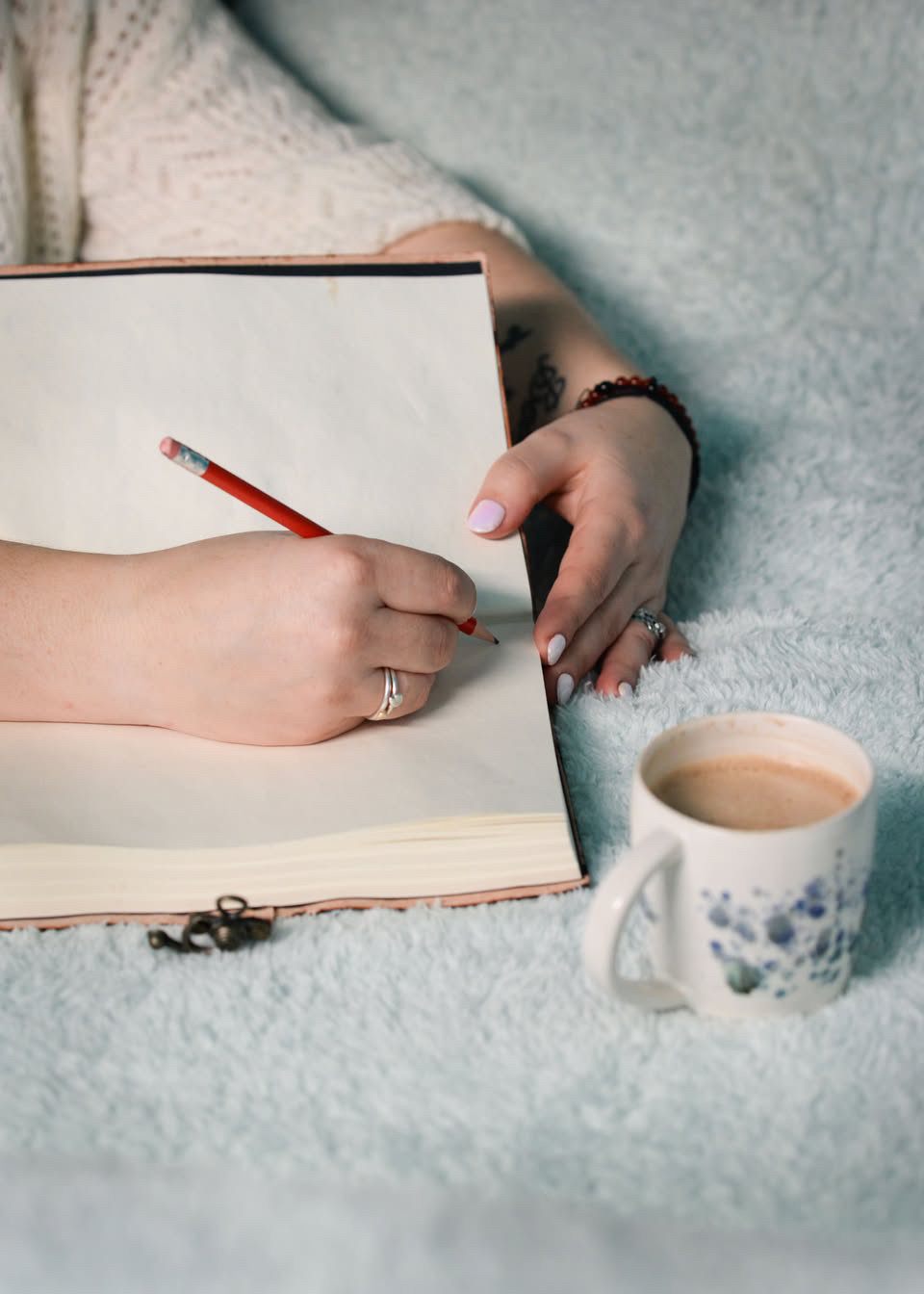 Hands writing in a leather journal beside a cup of coffee