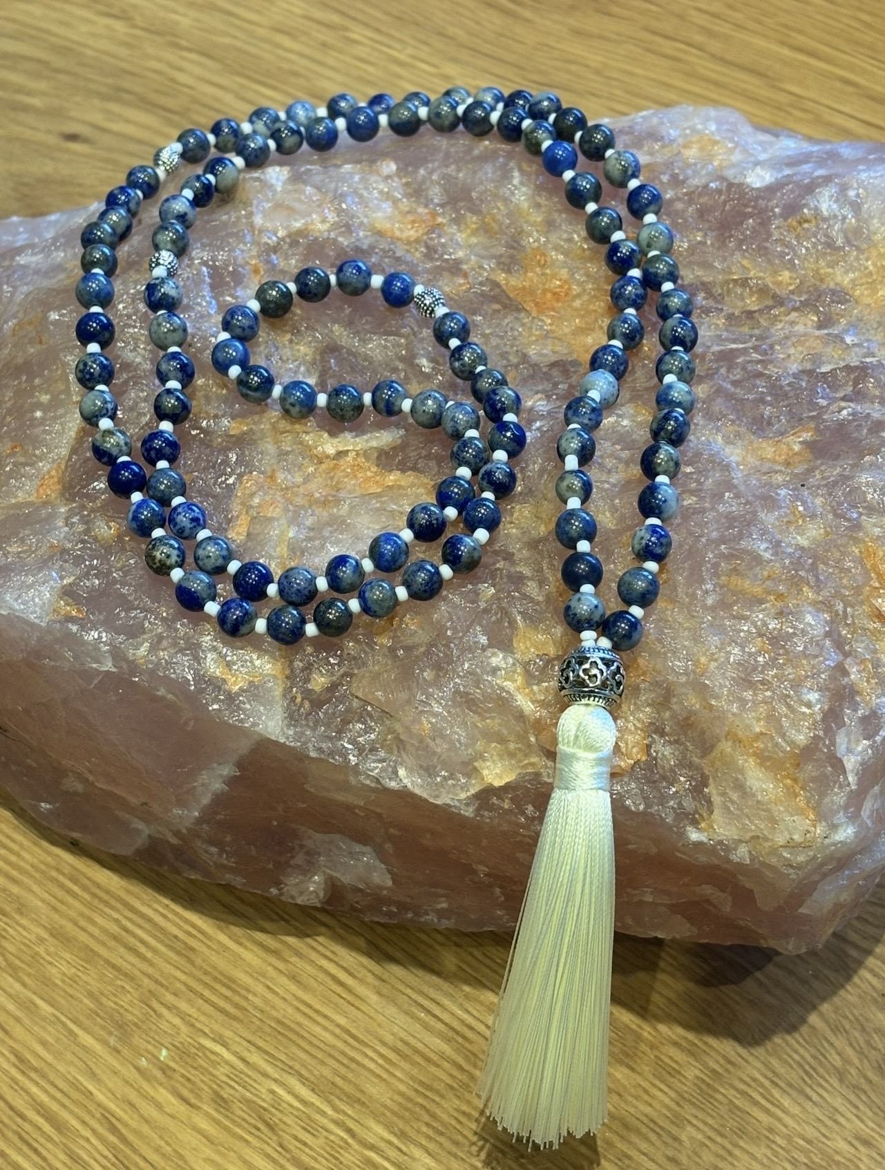 Handmade lapis lazuli mala necklace with a cream tassel, resting on rose quartz