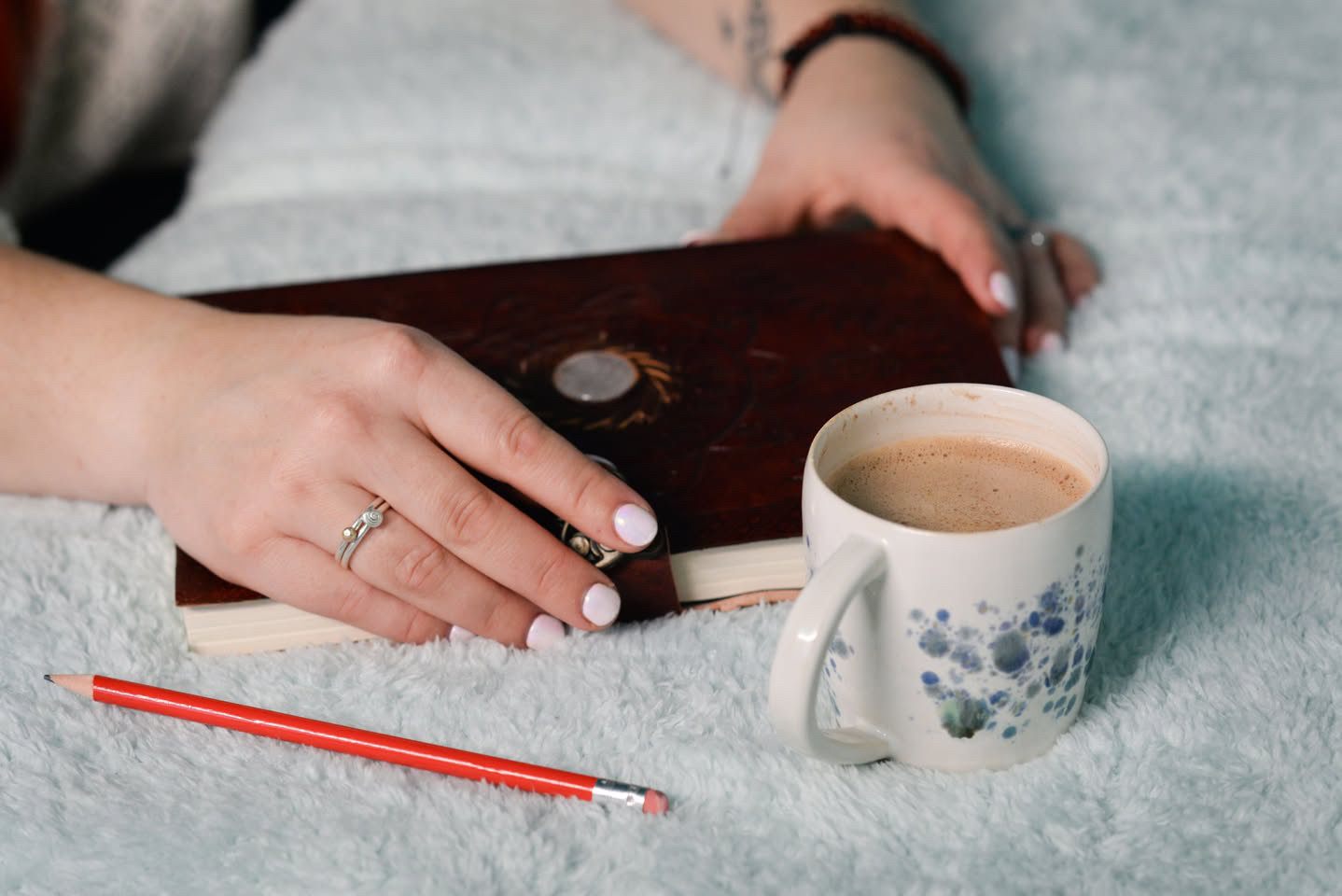A hand resting on a leather journal beside a cup of coffee, cosy and quiet