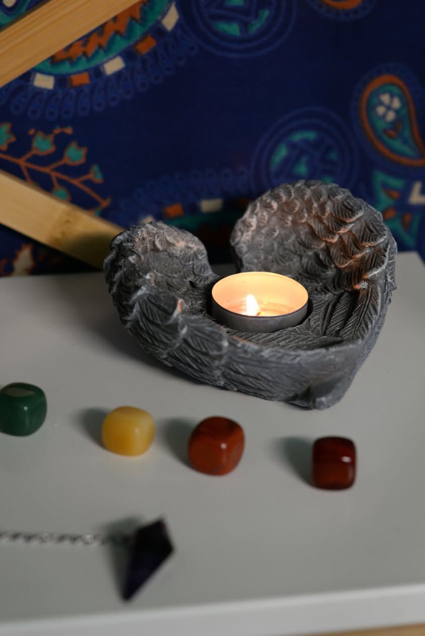 An angel-wing candle holder with a lit tealight, surrounded by tumbled crystals