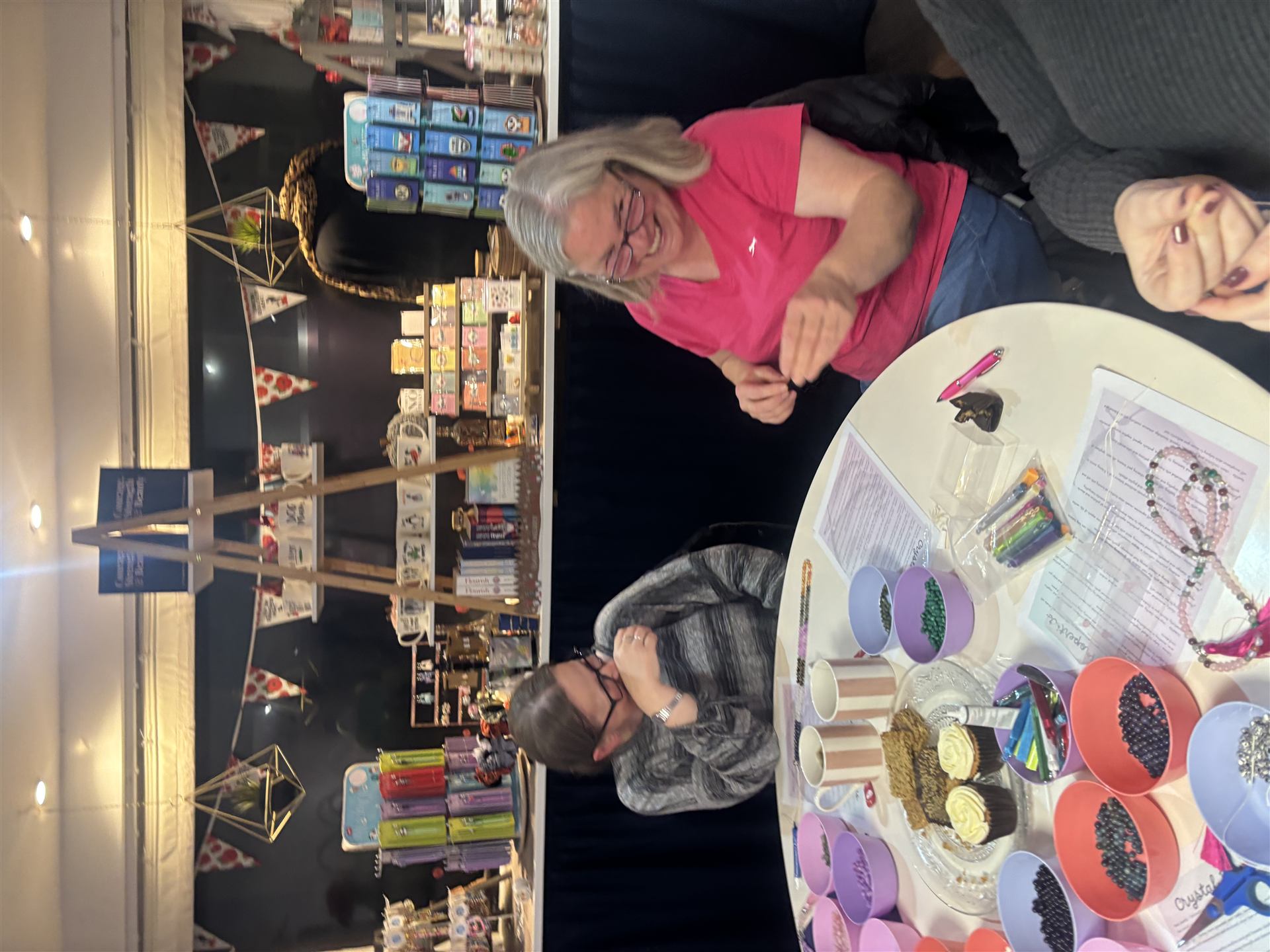Hannah laughing with a friend at a mala-making workshop table covered in bead bowls